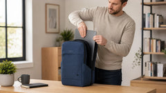 Man placing a laptop into a navy blue Purevave backpack at a desk